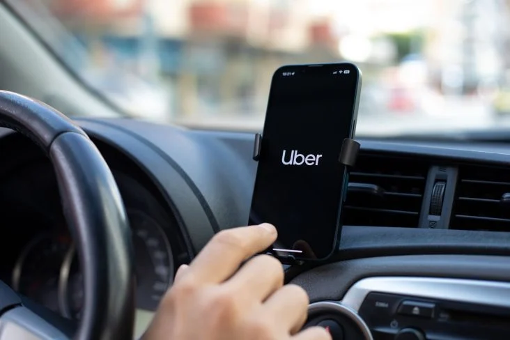 mao-de-pessoa-boa-clicando-em-celular-acom-logotipo-da-uber-afixado-em-painel-de-carro-lista-de-carros-uber-black-uber-comfort-2025-732x488